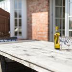 Outdoor area with table, wine bottle, and two glasses in front of brick wall and windows.
