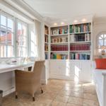 Home office with bookcase, windows, and seating bench.