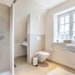Badezimmer mit Dusche, Toilette und Waschbecken. Fenster mit Blick auf Dächer.