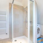 Dusche mit Duschbrause, Heizung und Waschmaschine im Bad