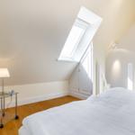 Schlafzimmer mit Dachschräge, Dachfenster, Bett und Nachttisch.
