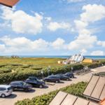 Parkplatz mit Autos und Blick auf das Meer und grüne Dünen.