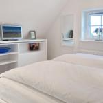 Bedroom with white bed, TV, and window with lamp.