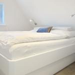 Bedroom with white bed, window, and table lamp.