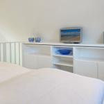 Bedroom with white bed and shelf. On the shelf are two bowls, a TV, and a picture frame.