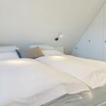 Bedroom with double bed, white bedding, and two wall lamps. A white wardrobe is against the wall.
