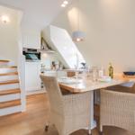 Dining area with table and chairs, kitchen, and staircase in background.