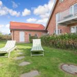 Green garden with two lounge chairs in front of a brick house under blue sky.