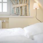 Bed with white linens, wall lamp, and window with checkered curtains.