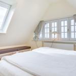 Bedroom with sloped ceiling, large window, and white bed.