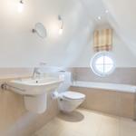 Bathroom with shower, sink, and toilet under sloped ceilings.