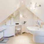 Bathroom with sink, mirror, and makeup station under sloped ceilings.