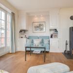 Living room with wooden floor, blue sofa, fireplace and large windows.