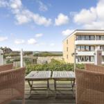 Terrace with two chairs and tables. View of buildings and beach.