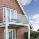 Red brick house with balcony and glass railing under blue sky.