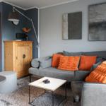 A living room with a gray sofa, orange cushions, and modern wall decor.