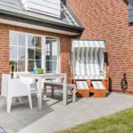 Terrace with table, chairs, and beach chair in front of brick house.