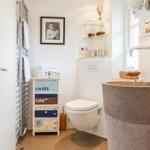 Badezimmer mit Steinwaschbecken, Toilette und Holzschrank mit Aufschrift.