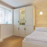 Schlafzimmer mit weißem Bett, Kleiderschrank und Fenster mit Jalousie.