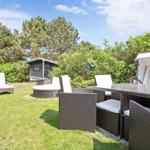 Garten mit Sitzgruppe, Sonnenschutz und Grillplatz. Hintergrund: Wald und kleine Hütte.