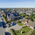 Haus mit Dachgauben und Solaranlage, umgeben von Grünflächen und einem Straßenzug mit Autos.