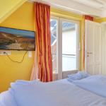 Bedroom with bed, TV, and window. Yellow walls and orange curtains.