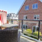 Terrace with lounge chair and table, view of brick house and garden.