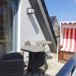 Terrace with two chairs, table, and beach chair. Background: house and clear sky.