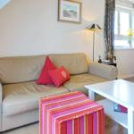 A living room with a light sofa, red cushions, and a colorful ottoman.