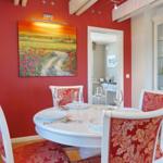 Red dining room with round table, chairs, and wall painting.