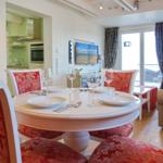 Round table with chairs, TV, and kitchen area in the background.