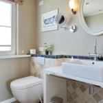 Bathroom with sink, mirror, and toilet. Window, wall art, and plant visible.
