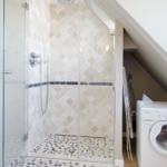 Shower with glass enclosure and washing machine under sloped ceiling