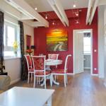 Dining area with table, chairs, and wall art. Wooden floor and ceiling beams.