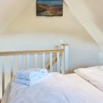 Two beds with white linens and towels under a dormer window.
