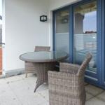 Terrasse mit Rattan-Tisch und Stühlen, Glas-Tür und weißer Wand.