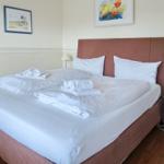 Ein Bett mit weißen Laken und Handtüchern. An der Wand hängen zwei Bilder.