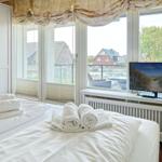 Zimmer mit Bett, TV und Blick auf Balkon mit Sitzgelegenheiten.