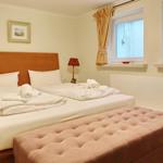 A bedroom with a double bed, windows, and a bench.