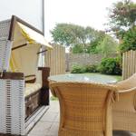 Terrace with rattan furniture and beach chair. Background: wooden fence and greenery.