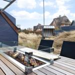 Terrace with fire pit, two chairs, and view of roofs and grass.