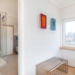 Shower area with glass wall and window with view of rooftops.