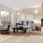 Living room with sofa, armchair, and fireplace. Wooden floor and large windows.