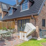 Haus mit Garten, Terrasse und Liegestuhl. Holzzaun und Steinmauer umgeben den Außenbereich.