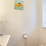 Badezimmer mit Waschbecken, Toilettenpapierhalter und Wandbild.
