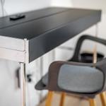 Schwarzer Schreibtisch mit Metallbeinen und Stuhl mit grauer Sitzfläche.
