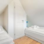 Zwei Betten mit weißen Bettwäsche und Handtüchern in einem Dachzimmer mit Holzboden und weißer Tür.