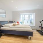 Schlafzimmer mit Bett, Spiegel, Fitnessrad und Fenster