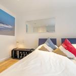 Schlafzimmer mit Bett, Kissen, Wandbild und Spiegel.