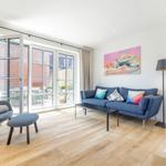 Wohnzimmer mit Sofa, Sessel, Kamin und Glasfront zur Terrasse.